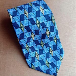 May include: A blue necktie with a geometric pattern. The tie features a repeating design of blue squares and triangles in varying shades, with accents of green and yellow. The tie is made of a smooth fabric and is suitable for formal occasions.