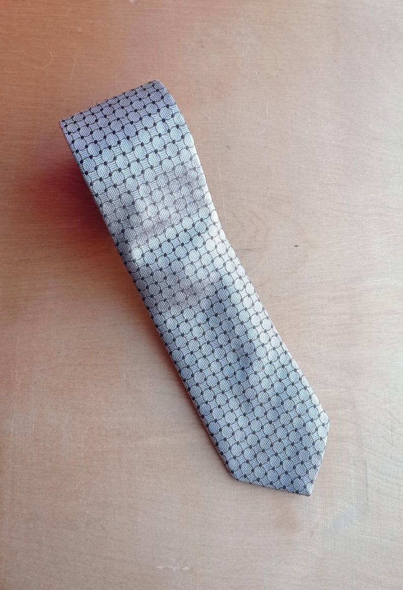 Vintage BAGOZZA MILANO necktie made in Italy from 100% pure silk. Features an elegant grey geometric pattern with a subtle sheen, representing classic Italian menswear design. This luxury tie is in great vintage condition, ideal for collectors or anyone seeking timeless formal accessories. Perfect for pairing with suits, businesswear, or dress shirts, this piece offers sophistication and heritage craftsmanship.