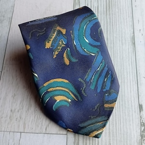 Könnte beinhalten: Eine marineblaue Krawatte mit einem sich wiederholenden Muster aus türkisfarbenen, hellblauen und goldenen abstrakten Formen. Die Krawatte ist aus einem glatten Stoff, möglicherweise Seide.
