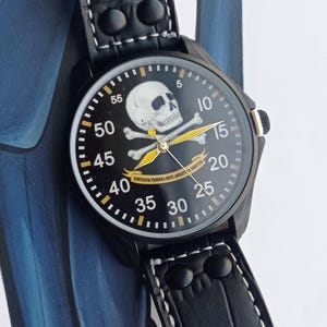 Men’s military quartz wristwatch inspired by the Spanish Army 8th Cavalry Regiment “Lusitania,” featuring a bold black dial with striking skull and crossbones emblem, a symbol of bravery, courage, and sacrifice. This collectible watch includes a precise quartz movement, durable black case, and a black leather strap with white stitching. Perfect for military history collectors, army enthusiasts, and men’s fashion lovers, this unworn timepiece represents unique heritage, bold design.