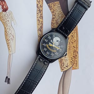 Men’s military quartz wristwatch inspired by the Spanish Army 8th Cavalry Regiment “Lusitania,” featuring a bold black dial with striking skull and crossbones emblem, a symbol of bravery, courage, and sacrifice. This collectible watch includes a precise quartz movement, durable black case, and a black leather strap with white stitching. Perfect for military history collectors, army enthusiasts, and men’s fashion lovers, this unworn timepiece represents unique heritage, bold design.