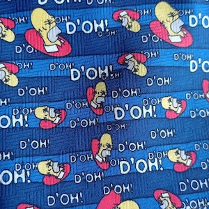 May include: Blue tie with a repeating pattern of Homer Simpson's face and the phrase "D'OH!" in white. The tie has a ribbed texture and a classic design, perfect for fans of the animated series.