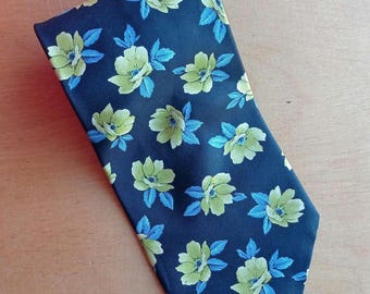 May include: A navy blue tie with a repeating floral pattern. The flowers are light green with yellow centers, and the leaves are blue. The tie is made of a smooth fabric and is suitable for formal or business attire.
