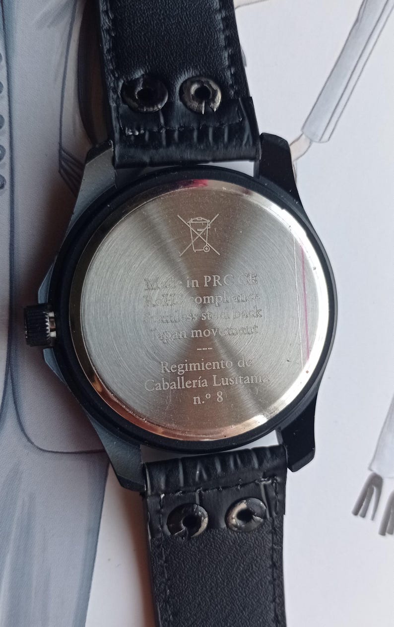 Men’s military quartz wristwatch inspired by the Spanish Army 8th Cavalry Regiment “Lusitania,” featuring a bold black dial with striking skull and crossbones emblem, a symbol of bravery, courage, and sacrifice. This collectible watch includes a precise quartz movement, durable black case, and a black leather strap with white stitching. Perfect for military history collectors, army enthusiasts, and men’s fashion lovers, this unworn timepiece represents unique heritage, bold design.