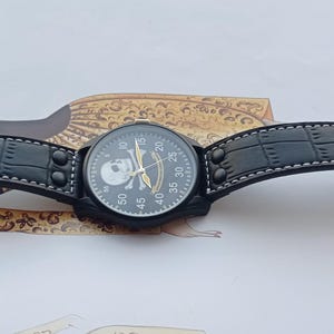 Men’s military quartz wristwatch inspired by the Spanish Army 8th Cavalry Regiment “Lusitania,” featuring a bold black dial with striking skull and crossbones emblem, a symbol of bravery, courage, and sacrifice. This collectible watch includes a precise quartz movement, durable black case, and a black leather strap with white stitching. Perfect for military history collectors, army enthusiasts, and men’s fashion lovers, this unworn timepiece represents unique heritage, bold design.