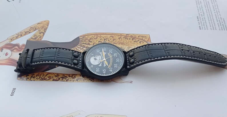 Men’s military quartz wristwatch inspired by the Spanish Army 8th Cavalry Regiment “Lusitania,” featuring a bold black dial with striking skull and crossbones emblem, a symbol of bravery, courage, and sacrifice. This collectible watch includes a precise quartz movement, durable black case, and a black leather strap with white stitching. Perfect for military history collectors, army enthusiasts, and men’s fashion lovers, this unworn timepiece represents unique heritage, bold design.