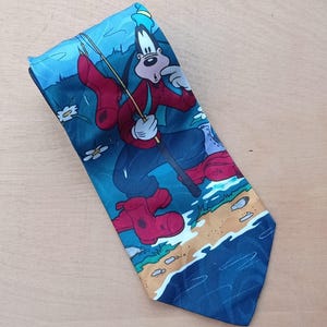 May include: A blue necktie with a cartoon illustration of Goofy fishing. Goofy is depicted in a red shirt, blue trousers, and red wellington boots. The background shows a blue lake, sand, and white flowers.