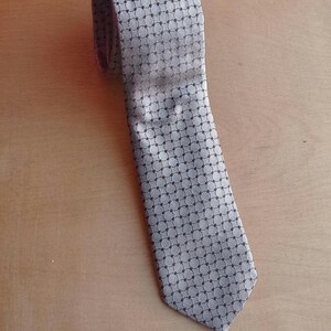 Vintage BAGOZZA MILANO necktie made in Italy from 100% pure silk. Features an elegant grey geometric pattern with a subtle sheen, representing classic Italian menswear design. This luxury tie is in great vintage condition, ideal for collectors or anyone seeking timeless formal accessories. Perfect for pairing with suits, businesswear, or dress shirts, this piece offers sophistication and heritage craftsmanship.