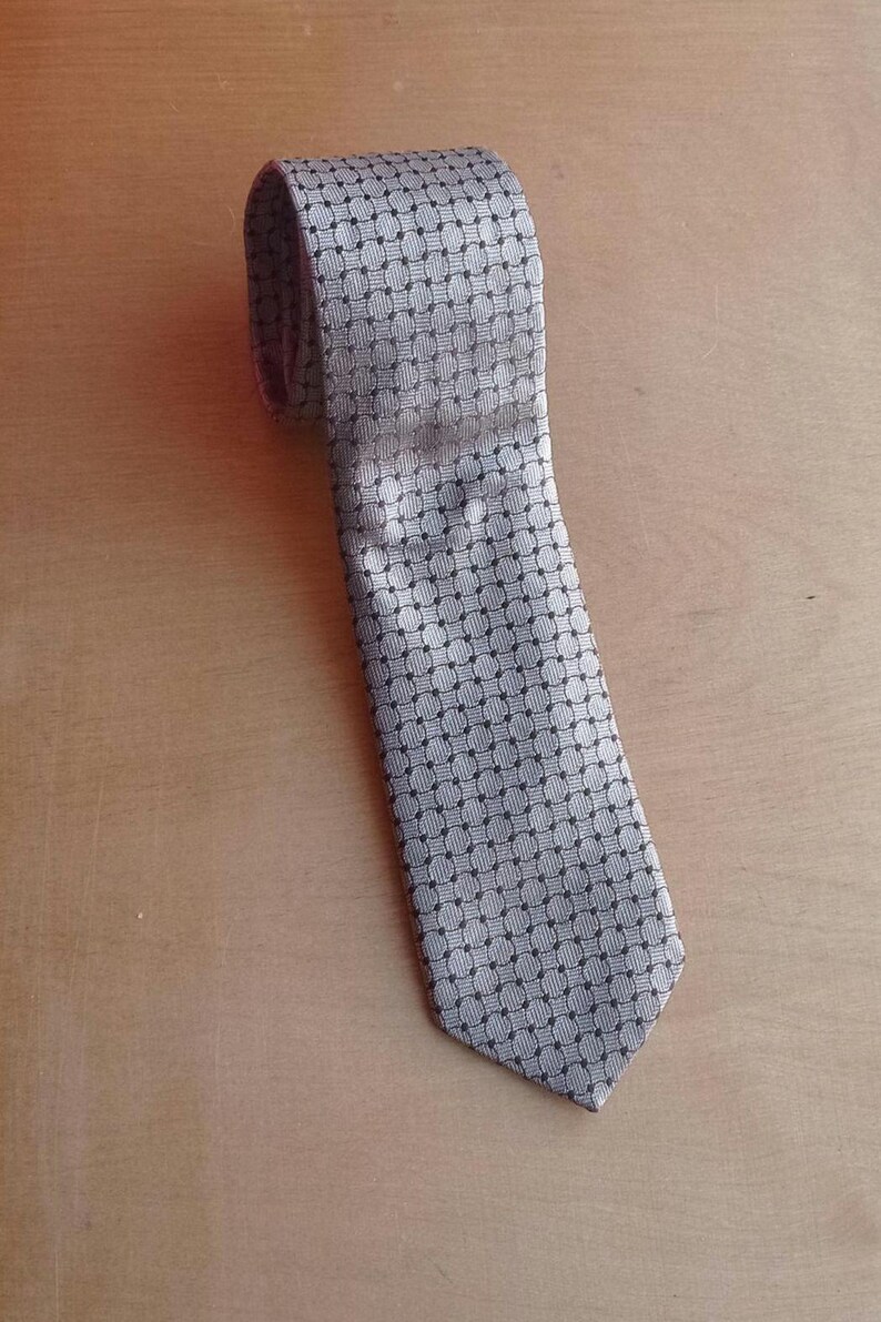 Vintage BAGOZZA MILANO necktie made in Italy from 100% pure silk. Features an elegant grey geometric pattern with a subtle sheen, representing classic Italian menswear design. This luxury tie is in great vintage condition, ideal for collectors or anyone seeking timeless formal accessories. Perfect for pairing with suits, businesswear, or dress shirts, this piece offers sophistication and heritage craftsmanship.