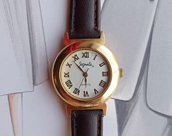 Reloj de cuarzo vintage Segnale para mujer: caja dorada, números romanos, esfera blanca, estilo clásico de la época.