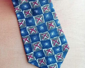 Puede incluir: Una corbata azul con un patrón repetitivo de cuadrados. Cada cuadrado contiene un fondo gris con un diseño de "X" rojo. La corbata está hecha de una tela suave y es adecuada para vestimenta formal o de negocios.