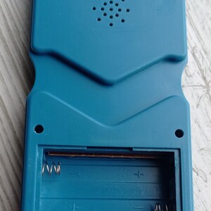 Close-up photo of a vintage WY-2007 Golden Light handheld console from the 1990s, featuring a blue body, purple buttons, and an LCD screen. The device offers 99 built-in games including Tetris. The packaging is aged, but the console itself is in new, unused condition. Perfect collectible for retro gaming fans and nostalgic 90s toy lovers.
