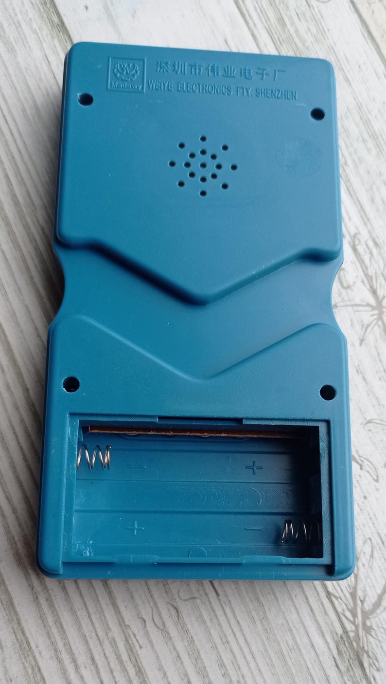 Close-up photo of a vintage WY-2007 Golden Light handheld console from the 1990s, featuring a blue body, purple buttons, and an LCD screen. The device offers 99 built-in games including Tetris. The packaging is aged, but the console itself is in new, unused condition. Perfect collectible for retro gaming fans and nostalgic 90s toy lovers.