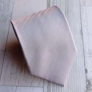 May include: A light gray tie with a subtle herringbone pattern. The tie is made of a smooth fabric and has a classic pointed end. The tie is a formal accessory.