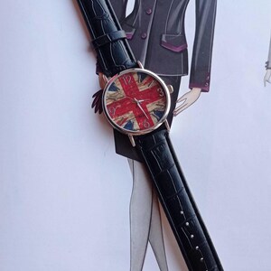 May include: A wristwatch with a black leather band and a round face featuring the Union Jack flag design in red, white, and blue. The watch has silver-colored hands and hour markers.