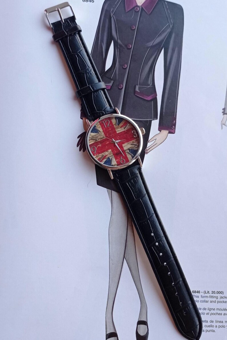 May include: A wristwatch with a black leather band and a round face featuring the Union Jack flag design in red, white, and blue. The watch has silver-colored hands and hour markers.