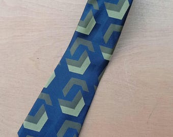 Puede incluir: Una corbata azul con un patrón geométrico repetitivo en tonos verdes y grises. La corbata está hecha de una tela suave y es adecuada para vestimenta formal o de negocios.