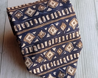 May include: Folded navy blue tie with a repeating pattern of tan and white geometric shapes. The tie has a diagonal stripe design with a repeating pattern of diamonds and rectangles.