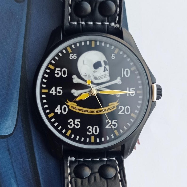 Men’s military quartz wristwatch inspired by the Spanish Army 8th Cavalry Regiment “Lusitania,” featuring a bold black dial with striking skull and crossbones emblem, a symbol of bravery, courage, and sacrifice. This collectible watch includes a precise quartz movement, durable black case, and a black leather strap with white stitching. Perfect for military history collectors, army enthusiasts, and men’s fashion lovers, this unworn timepiece represents unique heritage, bold design.