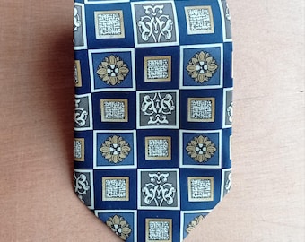 May include: A patterned necktie featuring a repeating square design. The squares are navy blue, with alternating floral and abstract patterns in gold, gray, and white. The tie is made of a smooth fabric.