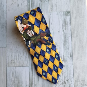 May include: A patterned necktie featuring a yellow and blue diamond design with a cartoon illustration. The tie has a repeating pattern of blue spade symbols. The cartoon illustration depicts a character in a green outfit.