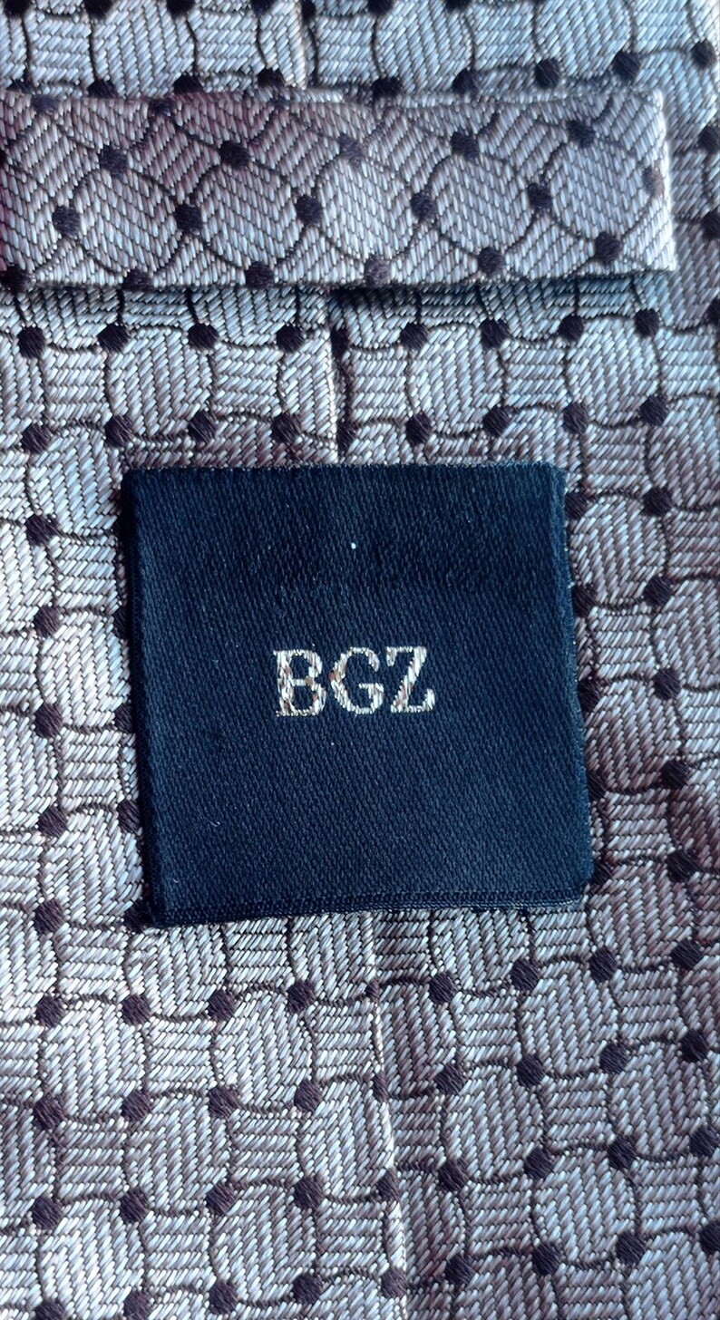 Vintage BAGOZZA MILANO necktie made in Italy from 100% pure silk. Features an elegant grey geometric pattern with a subtle sheen, representing classic Italian menswear design. This luxury tie is in great vintage condition, ideal for collectors or anyone seeking timeless formal accessories. Perfect for pairing with suits, businesswear, or dress shirts, this piece offers sophistication and heritage craftsmanship.