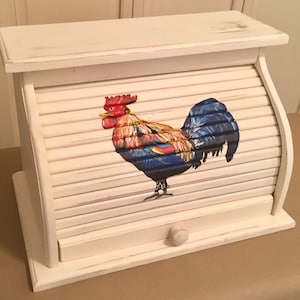 May include: White wooden bread bin with a rooster painted on the front. The bin has a roll-top lid and a small drawer.