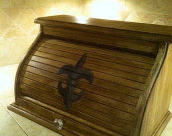 May include: A wooden bread bin with a distressed finish and a fleur-de-lis design. The bin has a hinged lid and a drawer with a crystal knob.