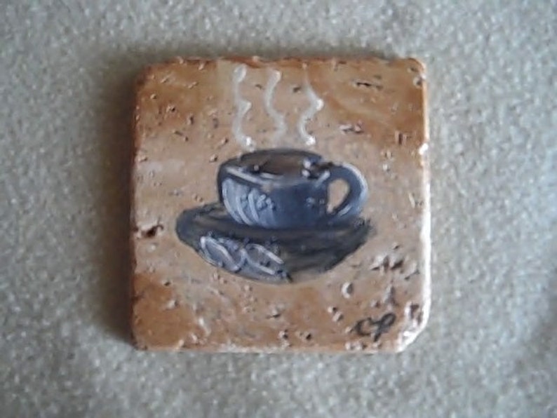 K&ouml;nnte beinhalten: Ein Keramik-Untersetzer mit einem gemalten Bild einer Tasse Kaffee, aus der Dampf aufsteigt.