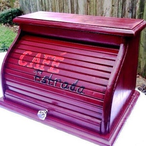 May include: A red wooden bread bin with a roll-top lid. The lid has a cafe sign that says "Cafe Estrada" in red and black lettering.
