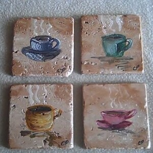 K&ouml;nnte beinhalten: Vier quadratische Untersetzer aus Keramik mit gemalten Bildern von Kaffeetassen. Jeder Untersetzer zeigt eine Tasse in einer anderen Farbe mit aufsteigendem Dampf. Die Untersetzer sind beige mit braunen Flecken.