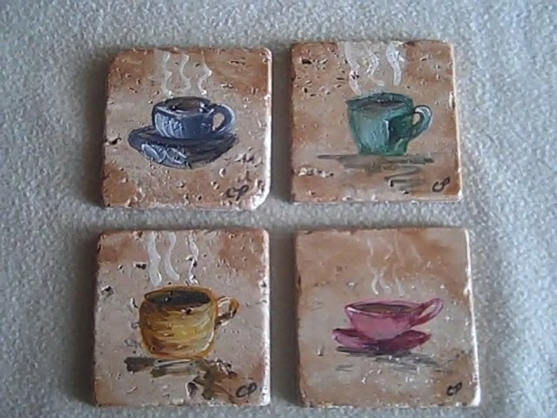 K&ouml;nnte beinhalten: Vier quadratische Untersetzer aus Keramik mit gemalten Bildern von Kaffeetassen. Jeder Untersetzer zeigt eine Tasse in einer anderen Farbe mit aufsteigendem Dampf. Die Untersetzer sind beige mit braunen Flecken.
