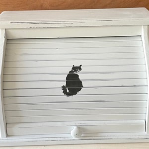 May include: White wooden bread box with a black cat silhouette design. The box has a roll-top lid and a small knob.