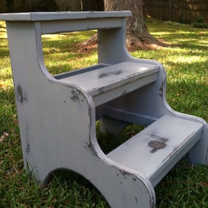 May include: A gray wooden step stool with two steps. The stool has a distressed paint finish and is made of solid wood.