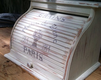 May include: White wooden bread bin with a roll-top lid. The lid has a distressed finish and is decorated with the text "Grains Moulin de Blanc 1914 Paris".
