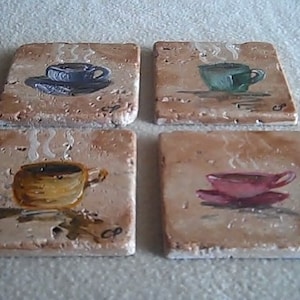 K&ouml;nnte beinhalten: Set aus vier quadratischen Untersetzern aus Keramik mit gemalten Bildern von Kaffeetassen. Jeder Untersetzer zeigt eine Tasse in einer anderen Farbe mit aufsteigendem Dampf. Die Untersetzer sind beige und haben eine raue Textur.