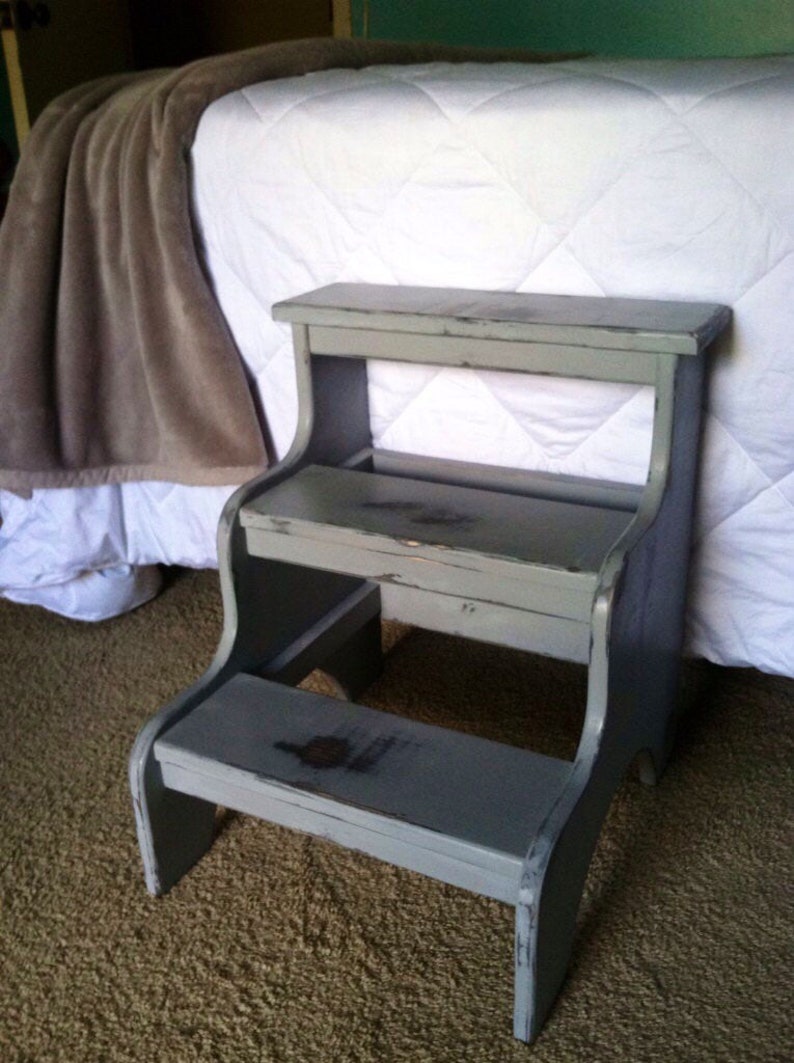 May include: A gray wooden step stool with two steps. The stool has a distressed finish and is slightly weathered.