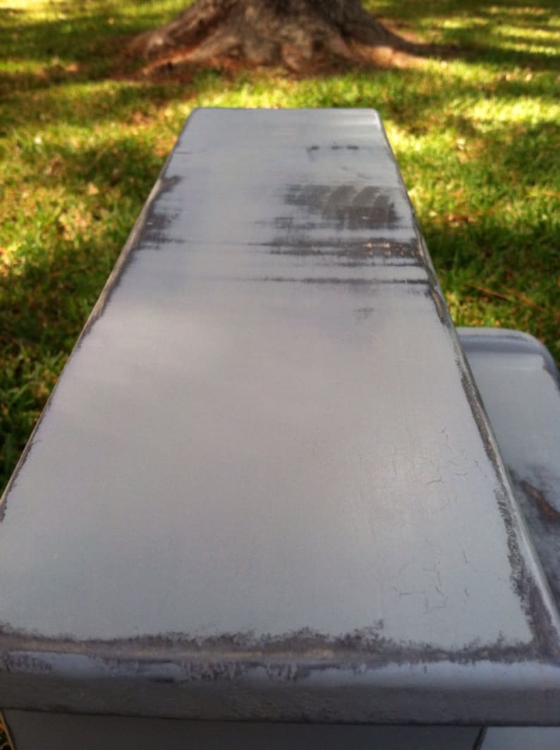 May include: A close-up of a gray painted wooden shelf with a distressed finish. The shelf has a smooth surface with visible brushstrokes and a slightly chipped edge.
