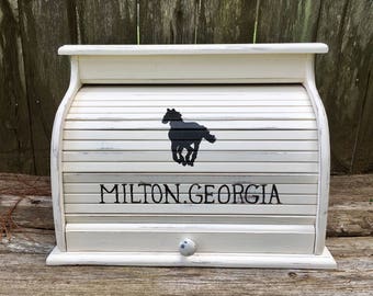 May include: White wooden bread box with a black silhouette of a horse running. The box has a roll-top lid and a small knob on the front. The text "MILTON, GEORGIA" is painted on the front of the box.