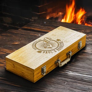 Può includere: Una scatola di legno con maniglia e testo inciso che recita "There's no barbecue like Paul's Barbecue". La scatola è in legno marrone chiaro e ha una chiusura metallica sul lato.