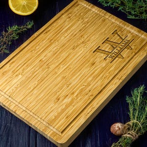 May include: A rectangular bamboo chopping board with a juice groove and engraved text. The text reads "L W WILLIAMS" in a stylized font. The board is light brown and surrounded by herbs and a lemon.
