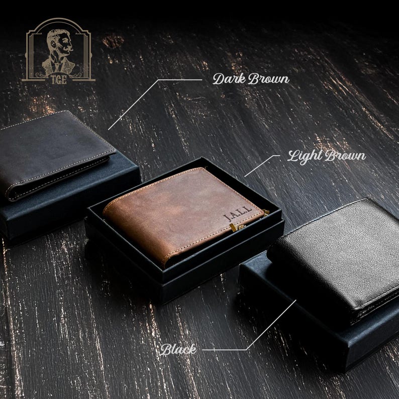 May include: Three leather wallets in different colors: black, dark brown, and light brown. The wallets are displayed on a wooden surface. The light brown wallet has the name "JALL" engraved on it.