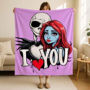 A woman is holding up a large pink blanket with a cartoon illustration of a skeleton and a woman's face on it.