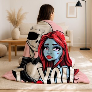 A woman is sitting on the floor, wrapped in a blanket with a cartoon-style illustration of a skeleton and a woman's face.