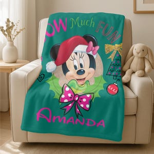 A green blanket with a Minnie Mouse design and the text "Amanda" printed on it, placed on a chair.