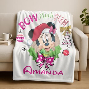 a white blanket with a Minnie Mouse design, along with various Christmas-themed elements such as a Christmas tree, ornaments, and a bow. The blanket has the text "BOW Much FUN Amanda" printed on it.