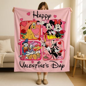 A woman is holding up a pink blanket with a collage of Disney characters and the text "Happy Valentine's Day" printed on it.