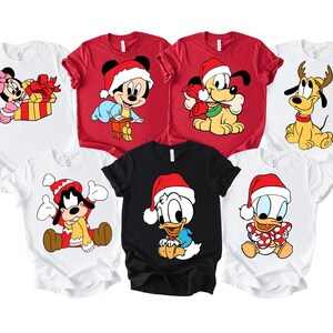 May include: A collection of white, red, and black t-shirts featuring various Disney characters in Christmas attire. Mickey Mouse, Minnie Mouse, Donald Duck, Pluto, and Goofy are depicted wearing Santa hats and festive outfits. The shirts are suitable for the holiday season.