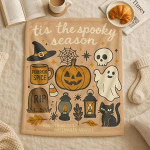 May include: A beige Halloween-themed blanket with various illustrations, including a jack-o'-lantern, witch's hat, skull, ghost, and black cat. Text on the blanket reads "'tis the spooky season", "Pumpkin Spice", "RIP", "Haunted Houses", and "Halloween Movies".
