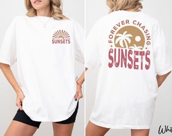 May include: White t-shirt with a sunset graphic on the front and back. The front features a sun and the word "SUNSETS". The back has a circular design with palm trees and the words "FOREVER CHASING SUNSETS".